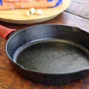 Lodge cast iron skillet with a red silicon handle cover on a wood table.